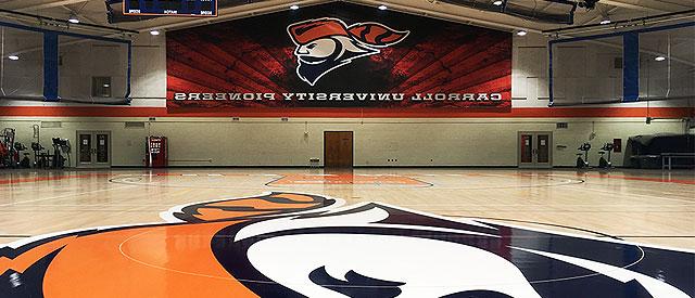 Image of the Van Male field house, where there is a glossy gym floor, basketball hoops, and the a larger Carroll Pioneers sign. 